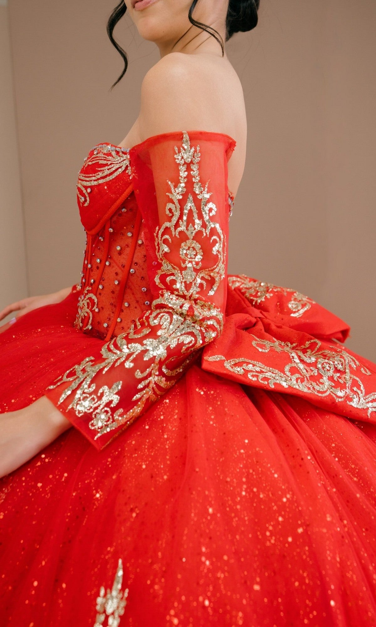 A woman wearing the Quinceanera Dress 8545JQ by Cinderella Couture, a red ball gown with gold embroidery, beaded sequins, off-the-shoulder sweetheart neckline, voluminous skirt, and detailed sleeves.